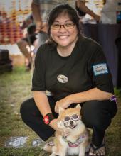 Photo of Nima Voices guest host Shari Y. Tamashiri, kneeling behind a cute, small dog.